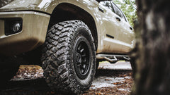 Close-up of a vehicle tire with off-road tread pattern on a forest path
