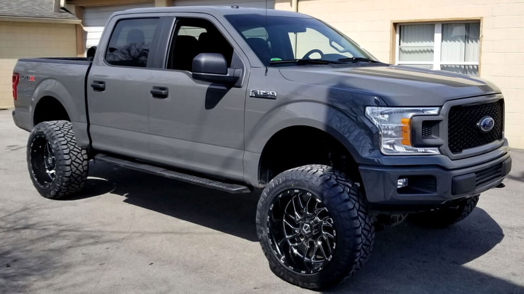 The gray Ford truck, with its large custom wheels, was parked on a concrete surface.