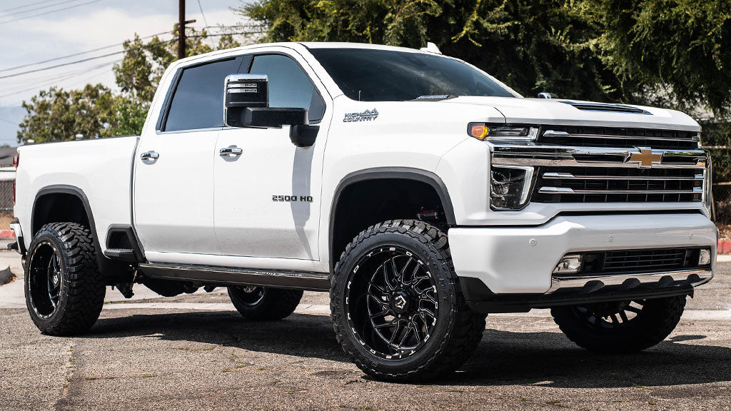 There is a white Chevrolet truck with black rims on a paved road.