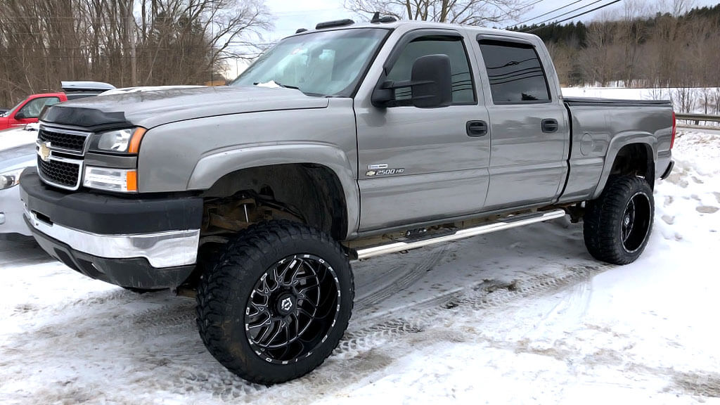 A Gray pickup truck with large black Custom wheels on a snowy surface