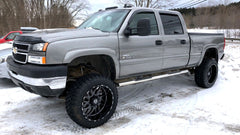A Gray pickup truck with large black Custom wheels on a snowy surface