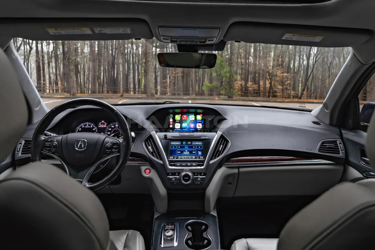 Car interior with dashboard and steering wheel, showing a forest outside.