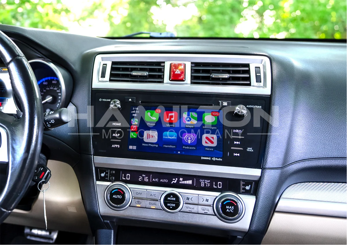 Car dashboard with a touchscreen display and various controls, brand 'subaru' visible.