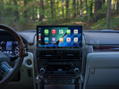 Car dashboard with a touchscreen display showing app icons, with a forest view outside.