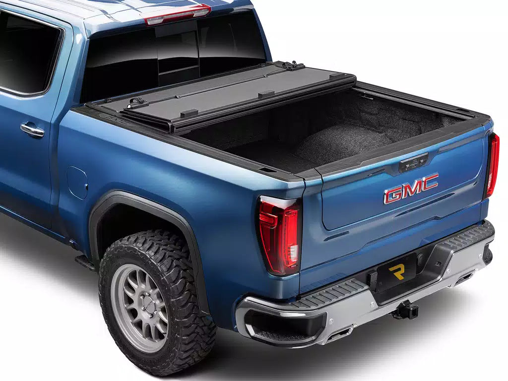 Blue GMC truck with a bakflip bed cover on a white background