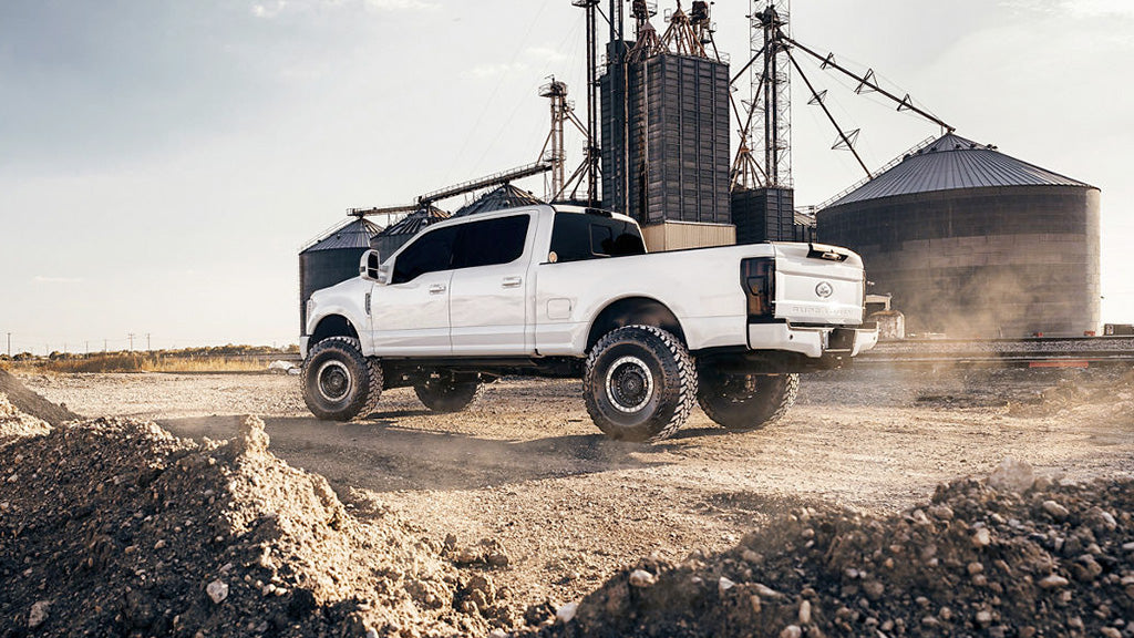White pickup truck on a dirt road with a grain silo in the background
