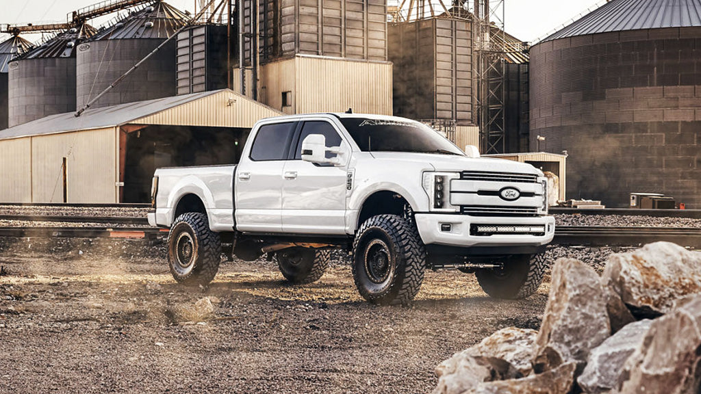 White pickup truck on a dirt road with industrial buildings in the background