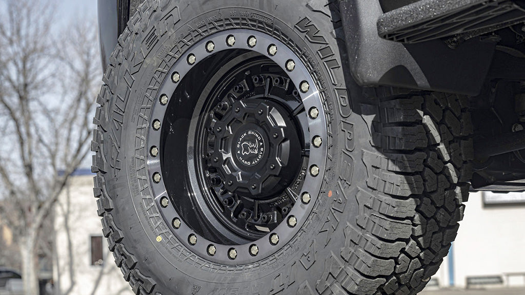 Close-up of a tire with a detailed tread pattern on a vehicle, set against an outdoor background.