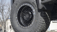 Close-up of a tire with a detailed tread pattern on a vehicle, set against an outdoor background.