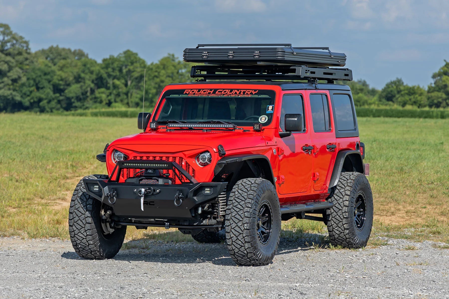 Red Jeep Wrangler with off-road equipment on a gravel road with grass and trees in the background