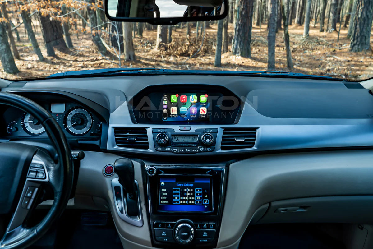 Car interior with dashboard and infotainment system displayed, surrounded by a forest.