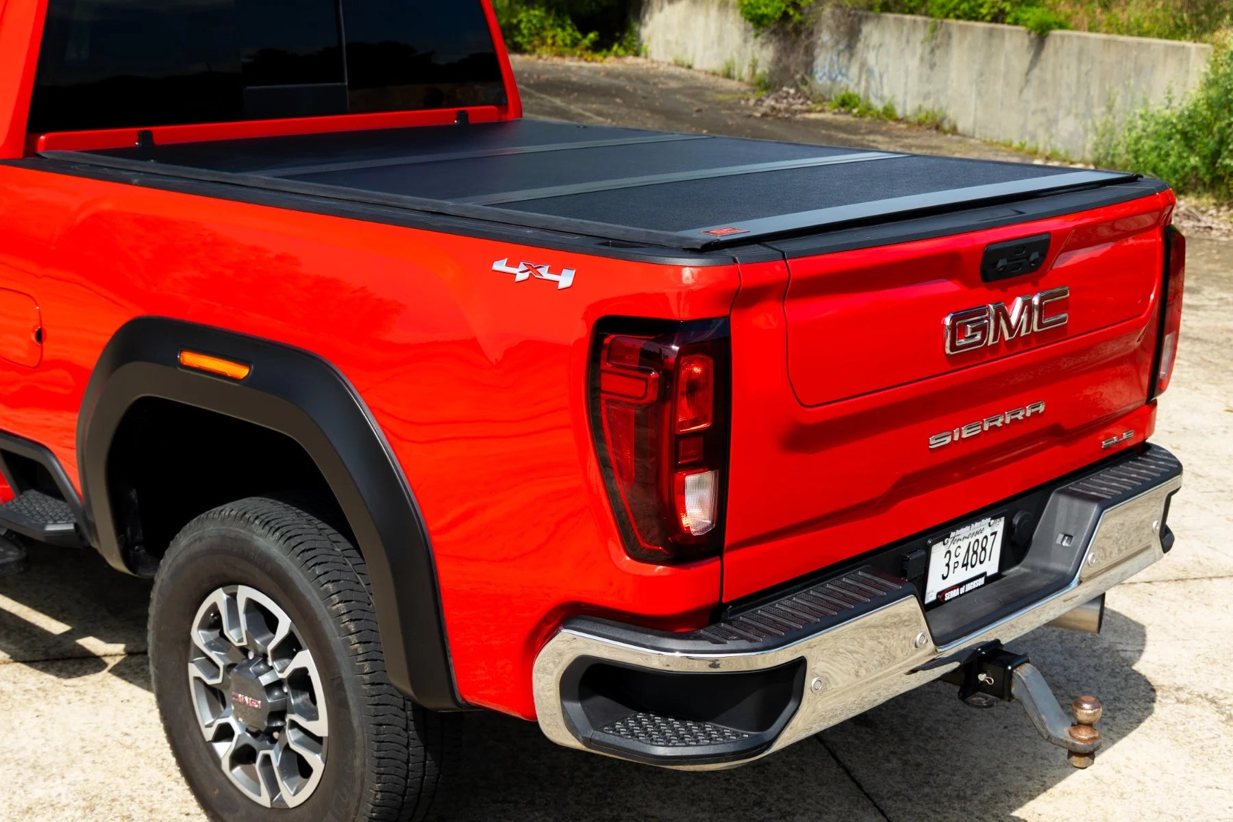 Red GMC truck with a tonneau cover on a concrete surface.