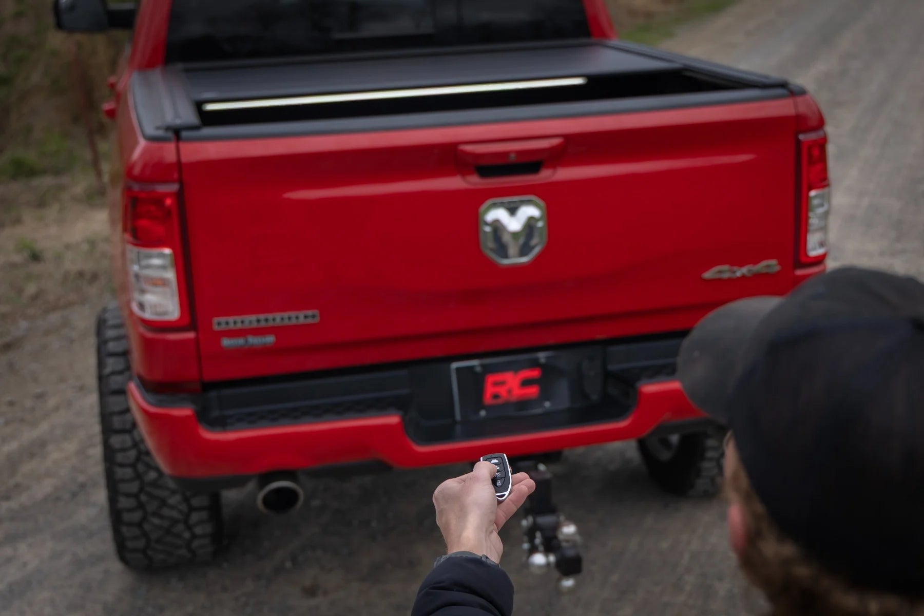 Red Ram truck with a person using a remote control to open the tailgate.
