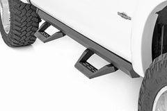 Close-up of a black step bumper on a white truck with rough country branding.
