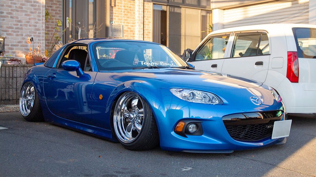 Blue sports car parked on a street with a white van in the background
