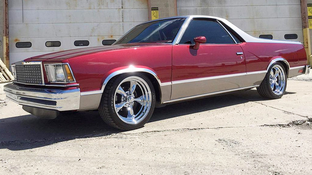 Red and silver classic car parked in front of a concrete wall.