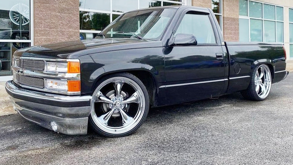 Black pickup truck with chrome rims parked on a street.