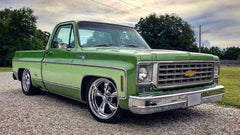 Green Chevrolet truck on a gravel surface with trees in the background
