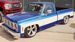 Blue and white pickup truck with chrome custom wheels details on a concrete surface.